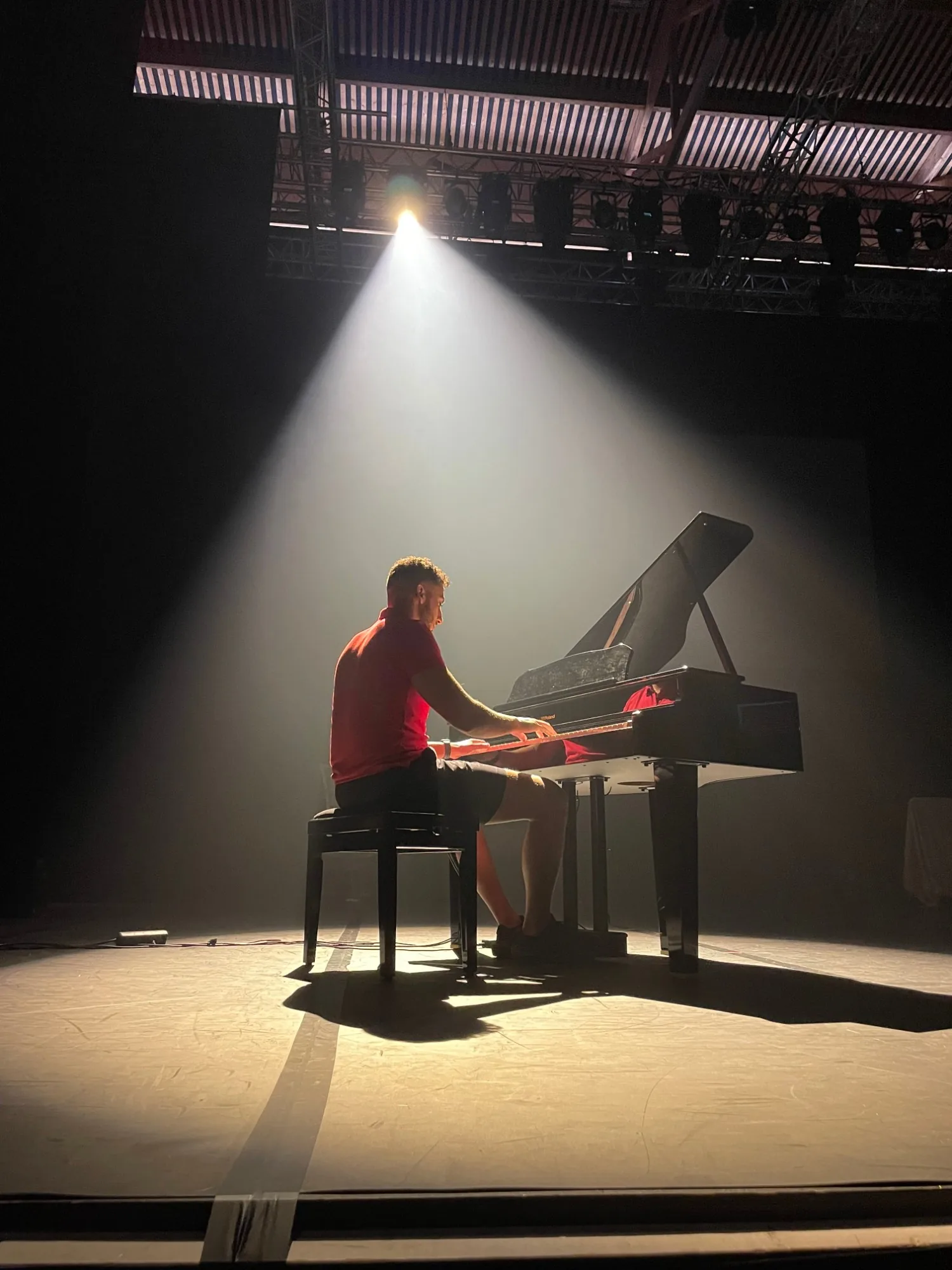 Adel Hakimi seul sur scène, au piano, sous un faisceau de projecteur.